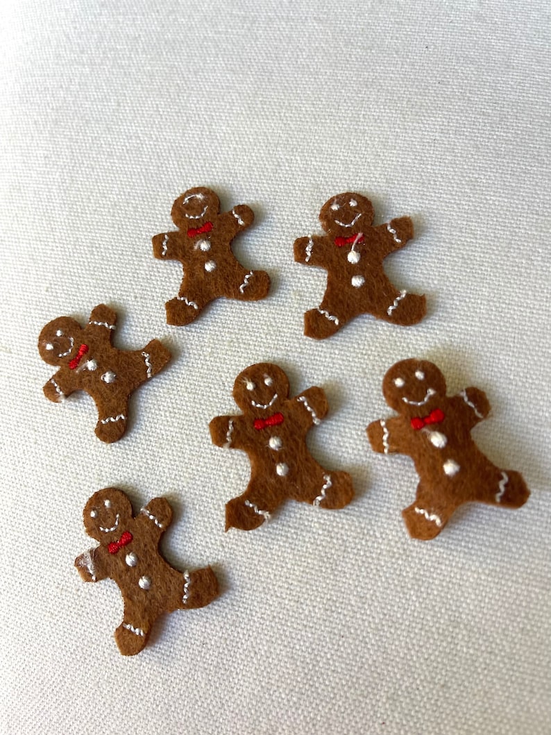 May include: Six brown felt gingerbread man ornaments with white icing details and red bow ties.