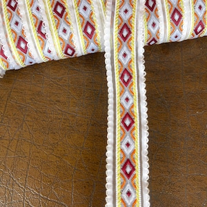 May include: White trim with a geometric pattern in shades of red, orange, and yellow. The trim has a scalloped edge.