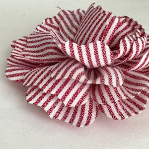 May include: A red and white striped fabric flower. The flower is made of multiple layers of fabric and has a ruffled edge.