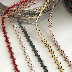 May include: Five spools of colorful trim with a zig-zag pattern and small beads. The trim is red, green, purple, yellow, and orange.