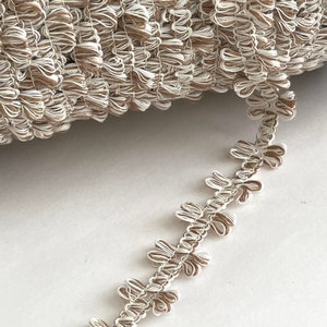 May include: A close-up of a spool of brown and white trim with a ruffled edge. The trim is made of a soft, textured fabric and is perfect for adding a touch of elegance to any project.