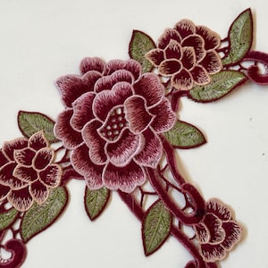 May include: Burgundy and green embroidered floral applique with three flowers and leaves. The applique is made of lace and has a delicate design.
