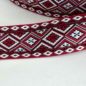 Könnte beinhalten: Nahaufnahme eines dekorativen Bandes mit einem sich wiederholenden geometrischen Muster. Das Band hat einen tiefroten Hintergrund mit weißen, schwarzen und roten Rautenformen. Das Design ist aufwendig und detailliert, geeignet für Bastelarbeiten.