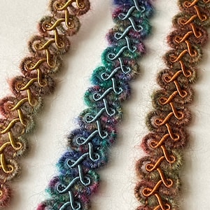 May include: Three strands of colorful braided trim with a fuzzy texture. The trim is made of a combination of yarn and satin ribbon. The colors are a deep teal, a muted orange, and a gold.