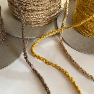 May include: Three spools of yarn in different colors: brown, beige, and yellow. The yarn is a thick, textured cord.