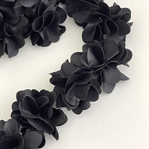 May include: Black floral trim with a delicate mesh backing. The trim is made of soft fabric and features a series of layered flower shapes.