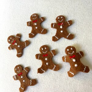 May include: Six brown felt gingerbread man ornaments with white icing and red bow ties.