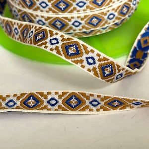 May include: White trim ribbon with a brown and blue geometric pattern. The pattern features repeating diamond shapes.