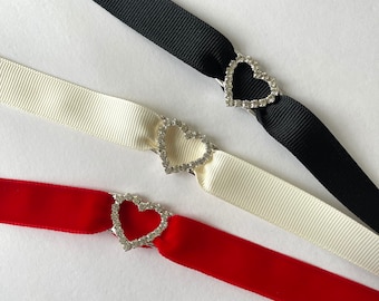 May include: Three ribbon choker necklaces with heart-shaped rhinestone clasps. The ribbons are black, white, and red.