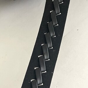 May include: Black leather strap with a braided design. The strap has a stitched edge and a woven pattern.