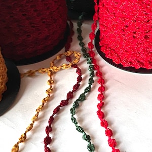 May include: Four spools of decorative trim, two red, one gold, and one green. The trim is made of twisted cord with small, knotted loops.