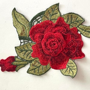 May include: Red embroidered rose with green leaves. This floral applique is perfect for adding a touch of elegance to clothing, crafts, or home decor.