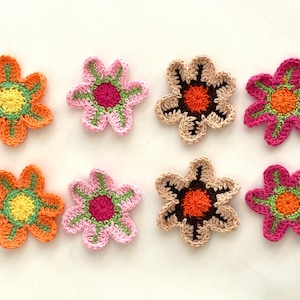 May include: Eight crocheted flower appliques in various colors, including pink, orange, brown, and green. Each flower has a center circle with a different color and pattern.