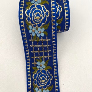May include: Blue and gold woven ribbon with a floral pattern. The ribbon features a repeating design of blue roses, small blue flowers, and gold gridwork.