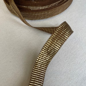 May include: Brown ribbon with gold metallic stripes. The ribbon is rolled up and a length is extended.