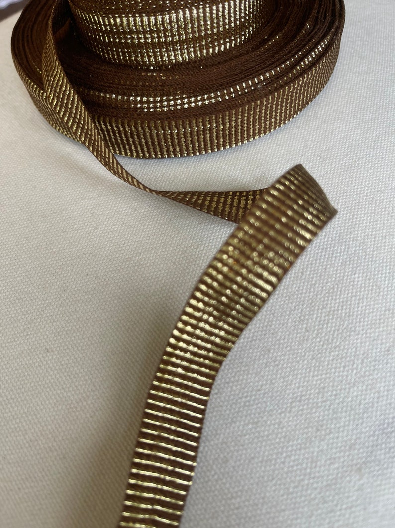 May include: Brown ribbon with gold metallic stripes. The ribbon is rolled up and a length is extended.