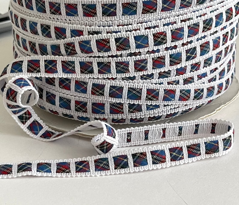 May include: White trim with a red, blue, and yellow plaid pattern. The trim is rolled up and shows the pattern repeating.