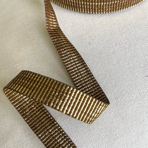 May include: Brown ribbon with gold metallic stripes. The ribbon is rolled up and a length is unfurled.