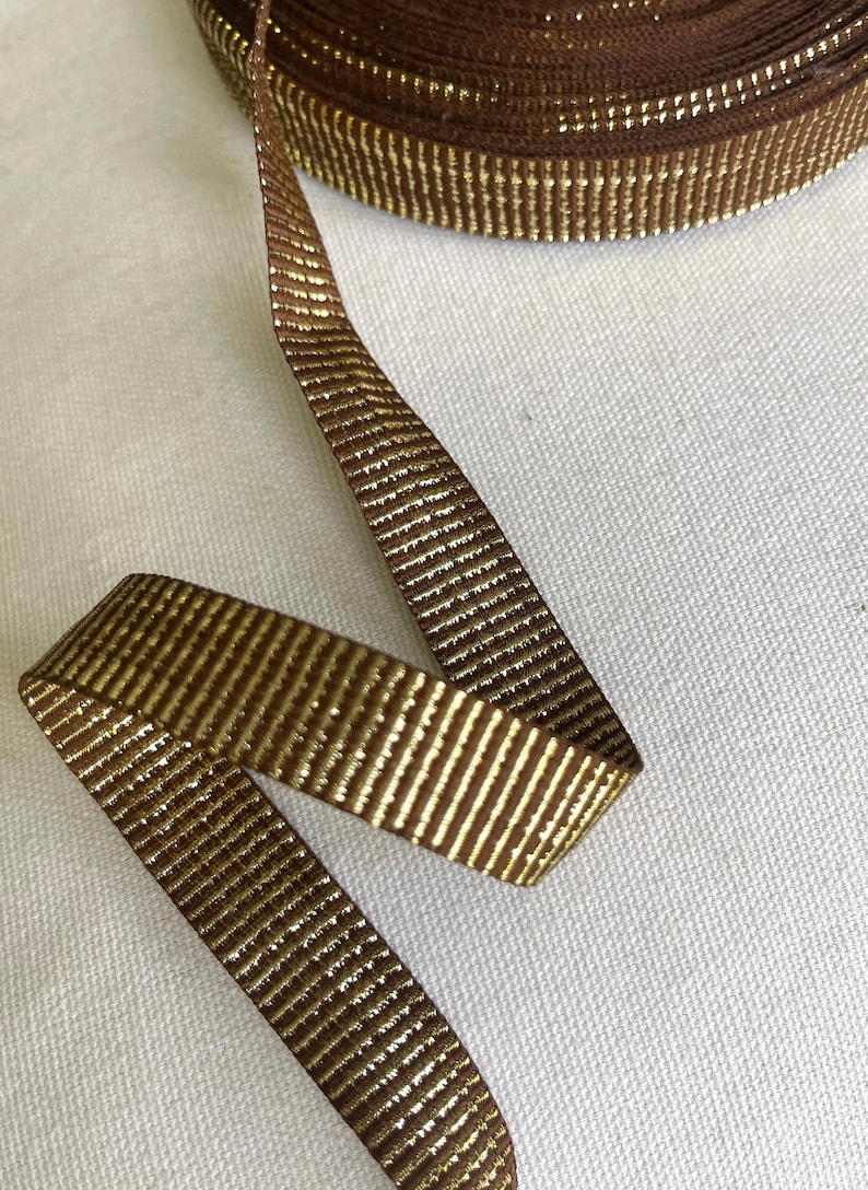 May include: Brown ribbon with gold metallic stripes. The ribbon is rolled up and a length is unfurled.