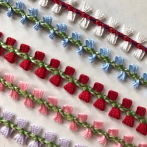 May include: Five rows of white, light blue, red, pink, and lavender trim with green and white accents. The trim is made of a woven fabric with small bows.