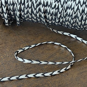 May include: Black and white braided trim with a chevron pattern. The trim is wound around a spool.