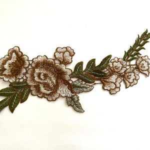 May include: A brown and white embroidered floral applique with green leaves. The applique features a large rose with smaller flowers and leaves.