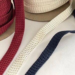 May include: Three spools of braided trim in red, cream, and navy blue. The trim has a textured, woven pattern.
