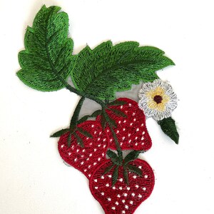 May include: Embroidered patch featuring three red strawberries with white seeds, a white flower with a yellow center, and green leaves.