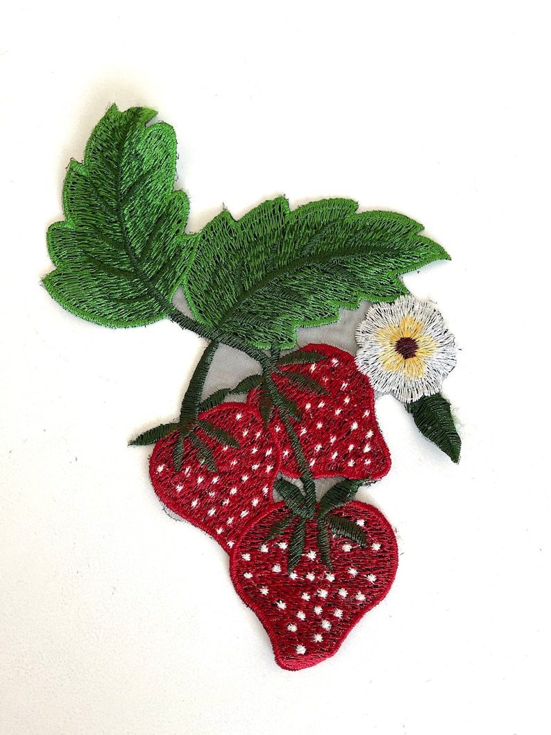 May include: Embroidered patch featuring three red strawberries with white seeds, a white flower with a yellow center, and green leaves.