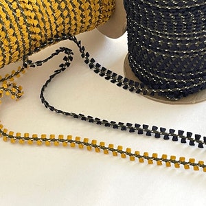 May include: Two spools of trim, one black and one gold, with a close-up of the trim laid out on a white surface. The trim is a scalloped design with a contrasting color thread running through it.
