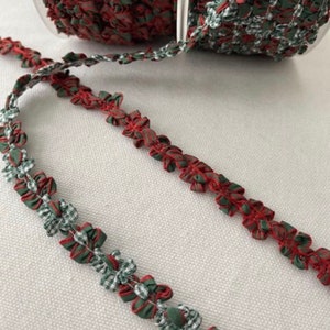 May include: Red and green gingham ribbon trim with a ruffled design. The ribbon is made of a soft, woven fabric and has a delicate, feminine look.