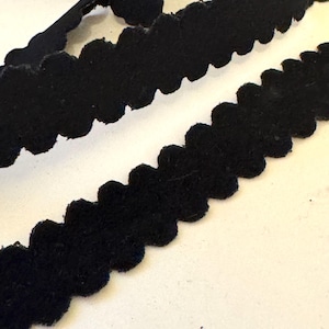 May include: Close-up of black scalloped trim. The trim has a soft, velvety texture and a wavy, decorative edge. The trim is likely used for sewing, crafting, or adding a decorative touch to clothing or accessories.