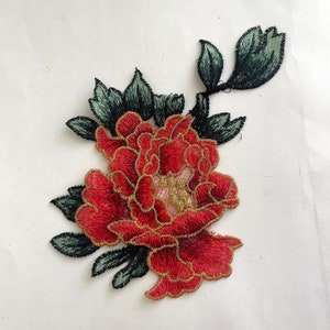 May include: Red embroidered flower applique with gold trim and green leaves.