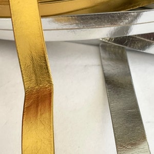 May include: Close-up of two rolls of metallic trim, one gold and one silver. The trim has a textured surface and is likely used for decorative purposes.