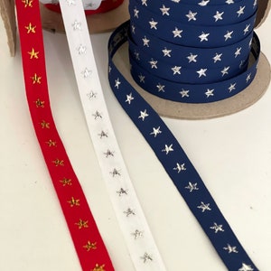 May include: Spools of ribbon in red, white, and navy blue, each adorned with star patterns. The red ribbon features gold stars, the white ribbon has silver stars, and the navy ribbon displays silver stars. Perfect for crafting and decorative projects.
