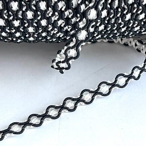May include: Black and white trim with a chain-like design. The trim is made of a woven fabric with a black cord running through it.