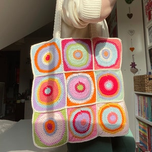 May include: A crocheted tote bag with a colorful geometric pattern. The bag is made of white yarn with circles of pink, orange, yellow, green, and blue.