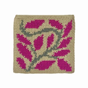 May include: A square, beige crocheted item with a repeating pattern of fuchsia-colored leaves and gray stems. The edges are finished with a beige border. The handmade item is likely a decorative pillow or a small blanket.