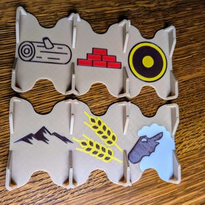 Puede incluir: Un conjunto de seis piezas de juego de plástico beige con diferentes imágenes. Las imágenes incluyen un tronco, un ladrillo, un objetivo, una montaña, trigo y una cabeza de oveja.