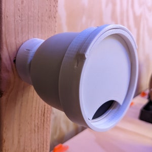 May include: White plastic vent cover with a round opening and a small, dark gray flap. The vent cover is mounted on a wooden surface.