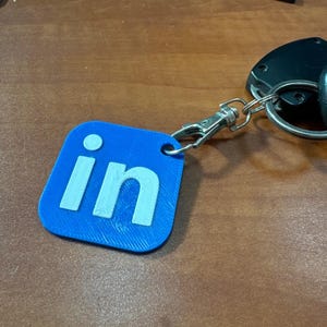 May include: A blue square keychain with the white text "in" on it.