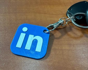 May include: A blue square keychain with the white text "in" on it.