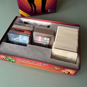 May include: A red and white game box with the words "Welcome to the Big Codenames Family" on the front. The box is open and contains a variety of game cards, including a set of clue cards, a set of code word cards, and a set of agent cards.