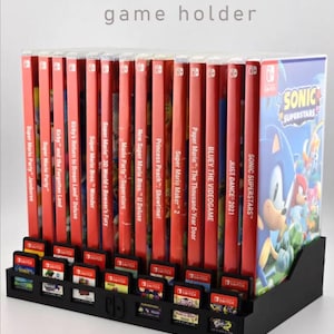 May include: Black Nintendo Switch game holder with multiple game cases and cartridges. The holder displays various game titles, including "Sonic Superstars" and "Just Dance 2021." The text "Available in various sizes" is at the bottom.