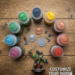 May include: A collection of nine round paint pots with colored lids featuring a winged emblem, several small grey plastic miniature components, and a painted green orc figurine holding a brush. The text CUSTOMIZE YOUR HORDE is visible.