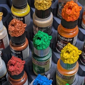 May include: A collection of paint bottles featuring custom 3D-printed bear head toppers in various colors including gold, silver, red, orange, green, yellow, and blue. The bear heads are mounted on the caps of acrylic paint bottles in a tray.
