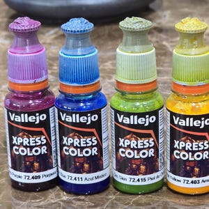 May include: Four Vallejo Xpress Color paint bottles in purple, blue, green, and yellow. Each bottle has a colored cap and a label with the brand name and color information. The bottles are for miniature painting and hobby use.