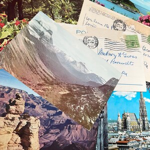 May include: A vintage postcard featuring a scenic mountain landscape with a snow-capped peak. The postcard is partially obscured by another postcard with handwritten text and a stamp dated July 14, 1939.
