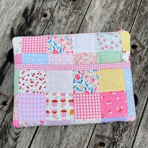 Könnte beinhalten: Eine Patchwork-Kosmetiktasche mit verschiedenen floralen und geometrischen Mustern in Rosa, Blau, Grün und Gelb.