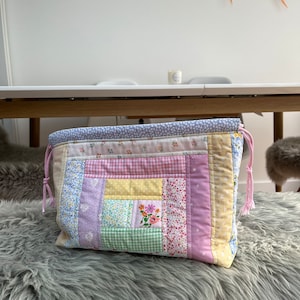 May include: A patchwork fabric drawstring bag with a pink, yellow, green, and blue floral pattern. The bag is made of different fabrics sewn together in a square pattern.